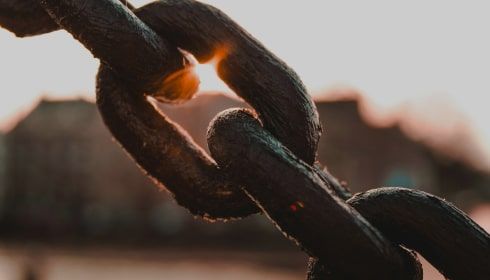 Close-up of heavy-duty steel chains with a warm sunset glow in the background, symbolising strength, interconnectedness, and industrial resilience.