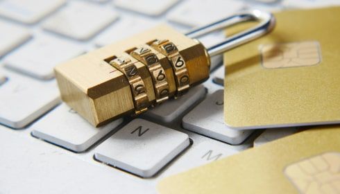 A combination lock resting on a computer keyboard next to a gold credit card, symbolising cybersecurity, data protection, and financial safety.