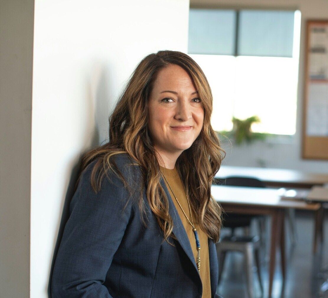 Confident professional woman in a business suit smiling at the camera, with a bright office setting in the background, portraying a positive work environment.