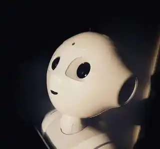 Don't let AI scams outsmart your business Close-up of a friendly-looking humanoid robot head with large eyes and a curious expression, set against a dark background, symbolising the approachability and advancement of artificial intelligence technology.