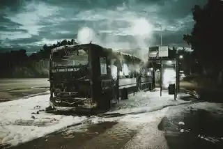 Burnt-out bus at night by roadside, foam-covered ground, eerie atmosphere, emergency aftermath.