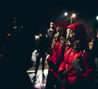 The cybercrime heist Masked individuals in red hoodies, resembling heist characters, creating a mysterious and suspenseful atmosphere at night. Cybercrime and security concepts.