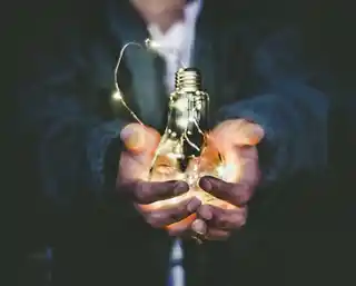 Hands cradling a lit bulb wrapped in fairy lights, symbolizing innovative ideas and creative solutions in darkness.