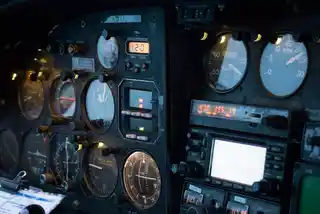 Close-up of an aircraft cockpit dashboard at dusk, showcasing an array of analogue gauges, dials, and digital screens, indicative of complex navigation systems.