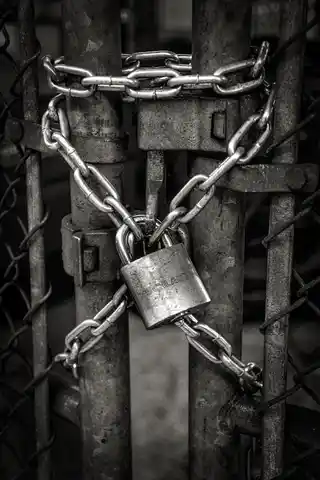 Why your password isn't enough A heavy-duty padlock securing a chain wrapped around a metal gate, captured in high-contrast black and white, symbolising strong security measures and the concept of safeguarding property.