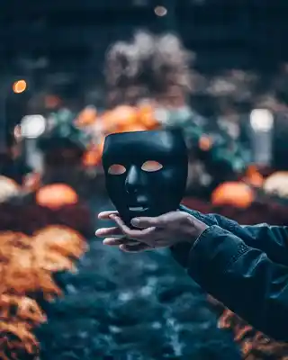 Person holding up a black theatrical mask in autumn setting, invoking mystery and drama themes.