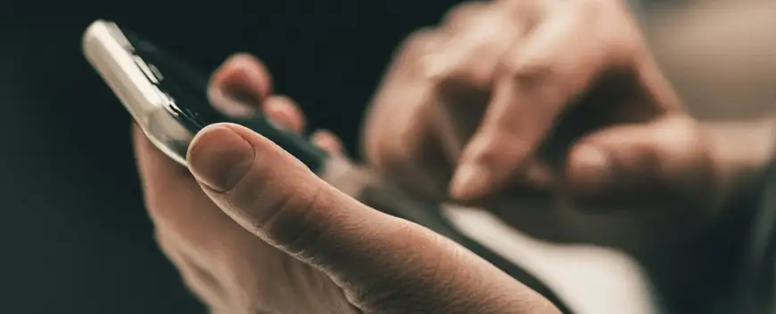 Close-up of a person's hands holding and typing on a smartphone, with a blurred background, focusing on the interaction with modern technology.