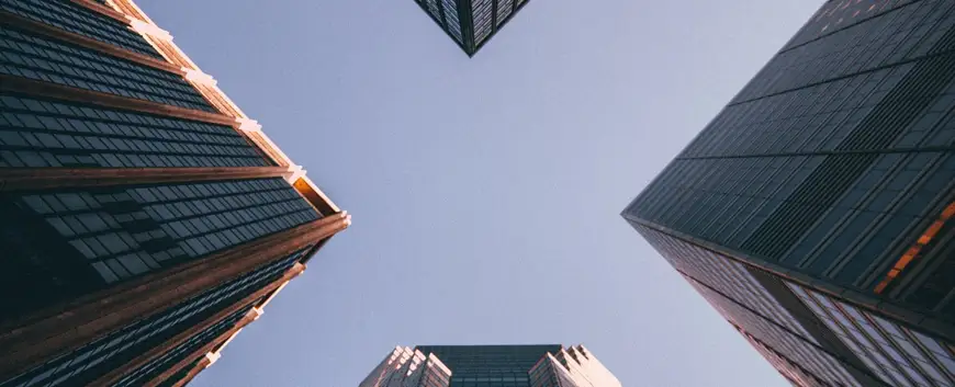 Worm's-eye view of towering skyscrapers converging against a clear sky, evoking a sense of corporate finance, economic power, and modern architectural design.
