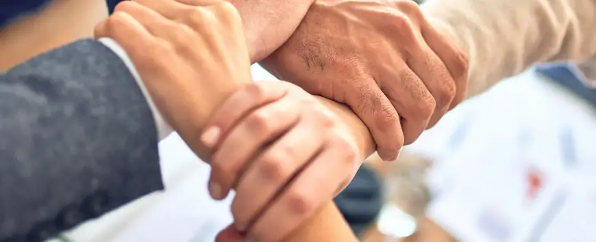 Close-up of a diverse team performing a hand stack to signify unity and teamwork, with a blurred background of a professional setting, emphasising collaboration in the workplace.